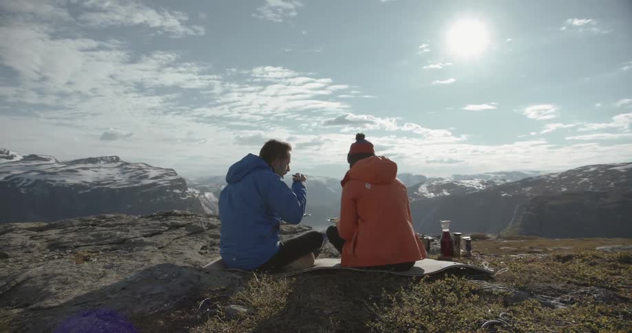 A man and woman have a picnic near the edge of a mountain top