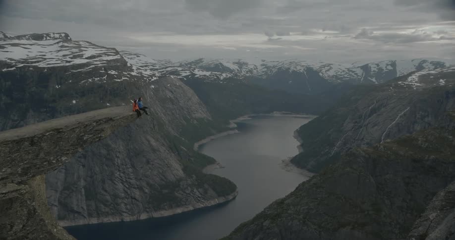 Two people are sitting on the edge of a steep cliff