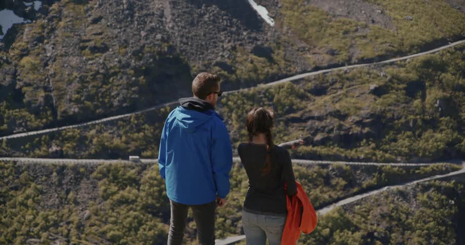 Man and woman looking out at view of mountain side with zigzag road
