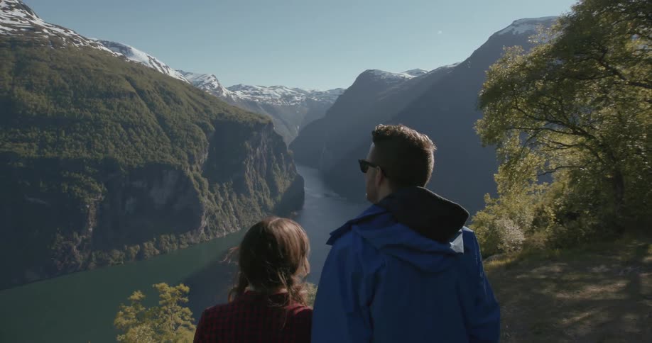 A man and women look over the edge of a cliff on a sunny day