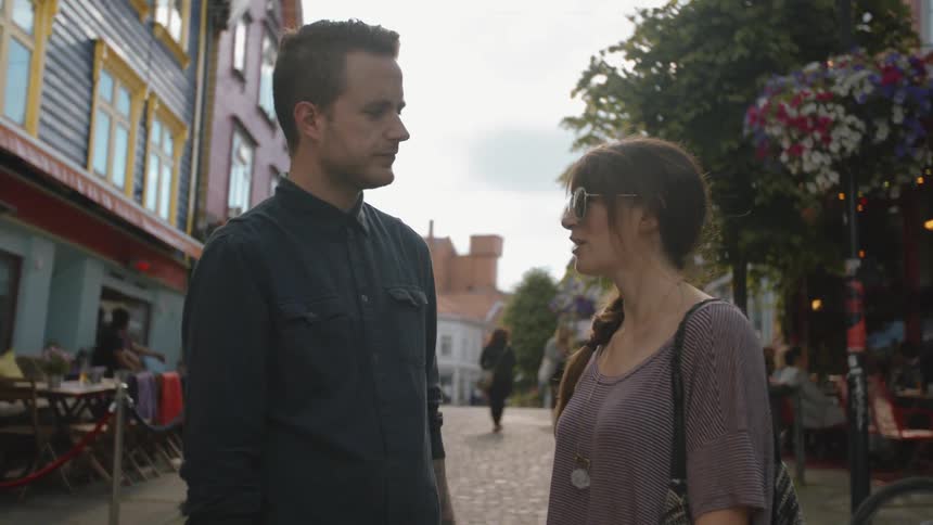 A man and woman talking on a street near a restaurant