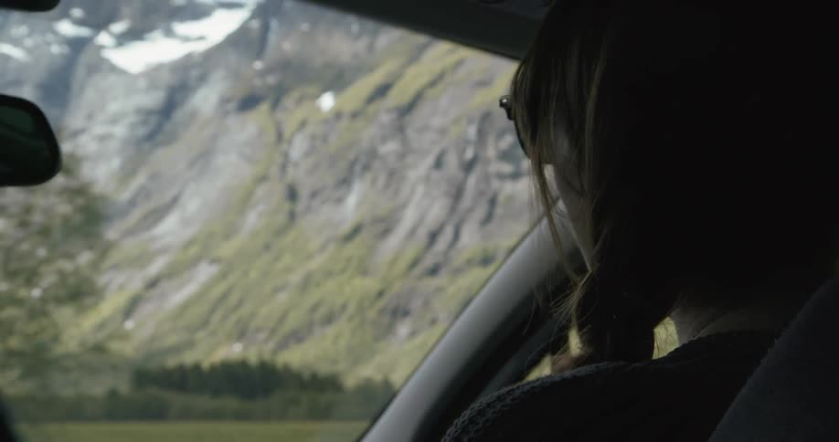 A female passenger smiling as she travels in a vehicle through the mountains