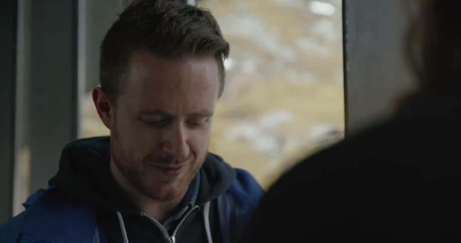 A man is sitting indoors talking to another person