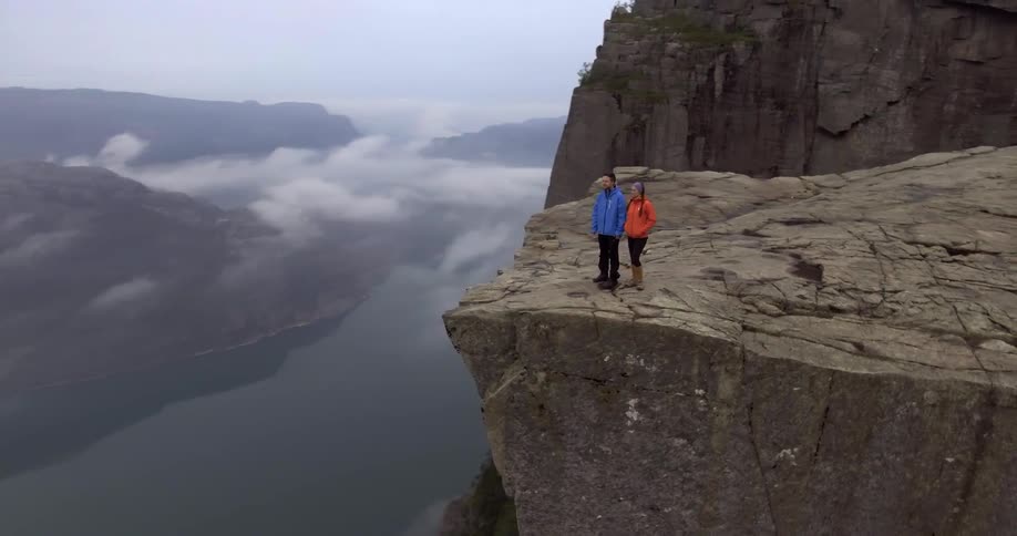 A man and woman stand at the edge of a mountain and overlook the river below