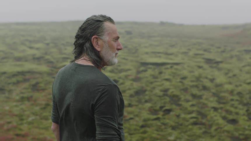 Long haired man standing on the green moss covered plains of the highlands
