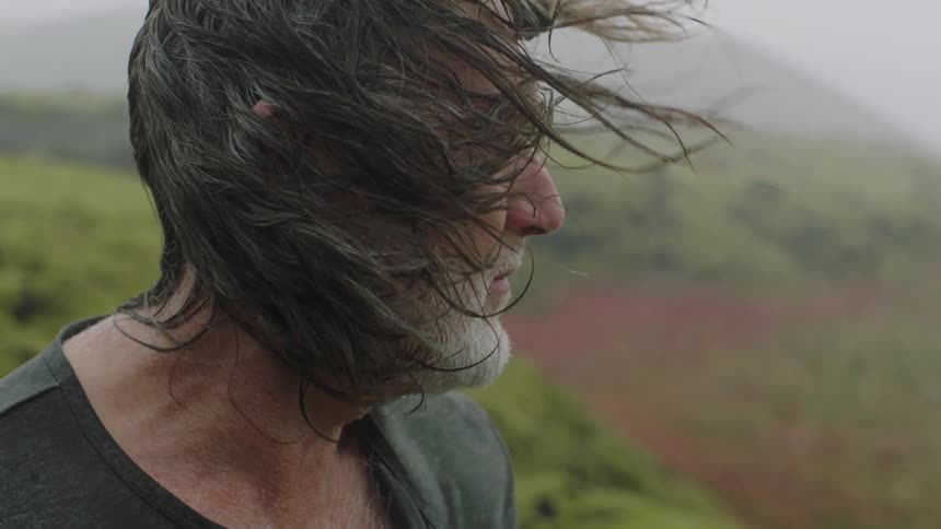 Wind blowing the long hair of a senior citizen standing on the moss covered hills of the highlands