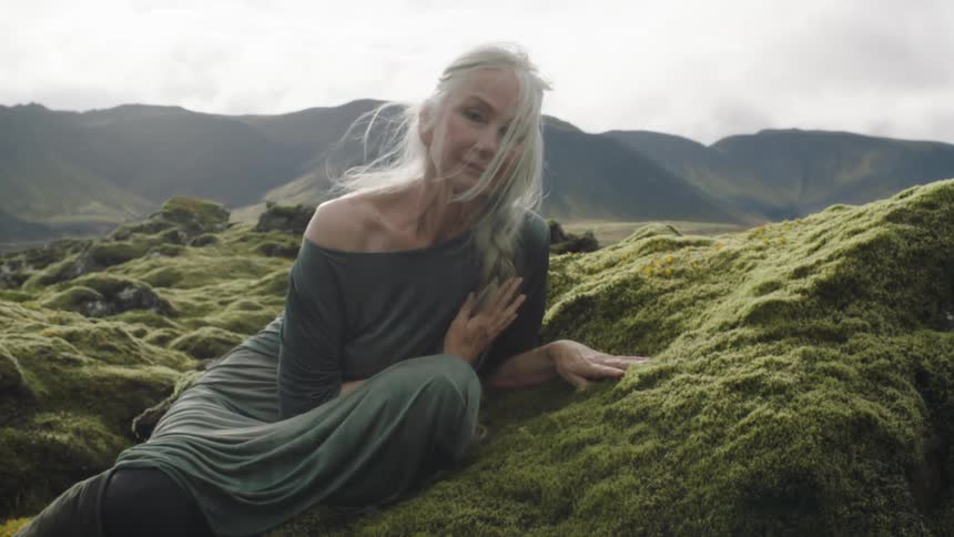 An elderly woman sitting on hill covered in moss