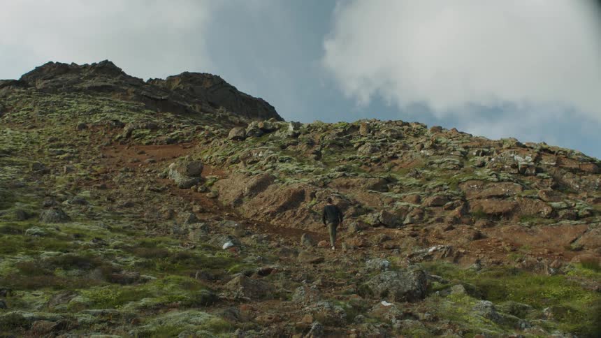 A man walks on a dirt path up an incline of a hill