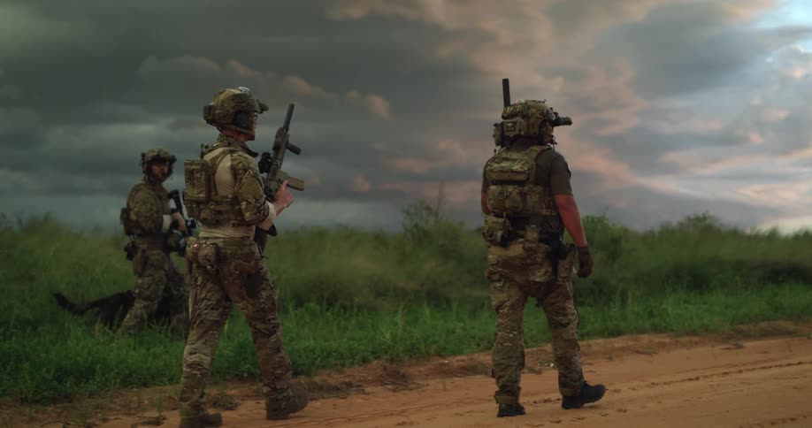 Military men searching on a dirt road in a rural area with a dog