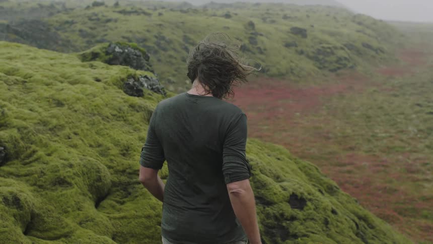 Long haired man walking down the moss covered hills in the highlands under the rain