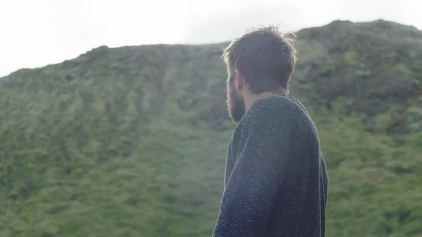 Caucasian man in a gray sweater look down then looking up at a mountain