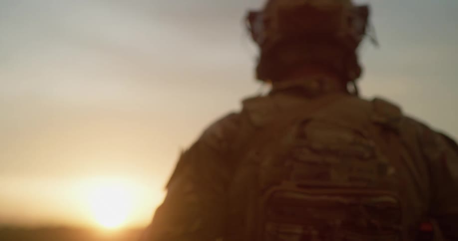 Soldier in full military gear walking to the horizon at sunset
