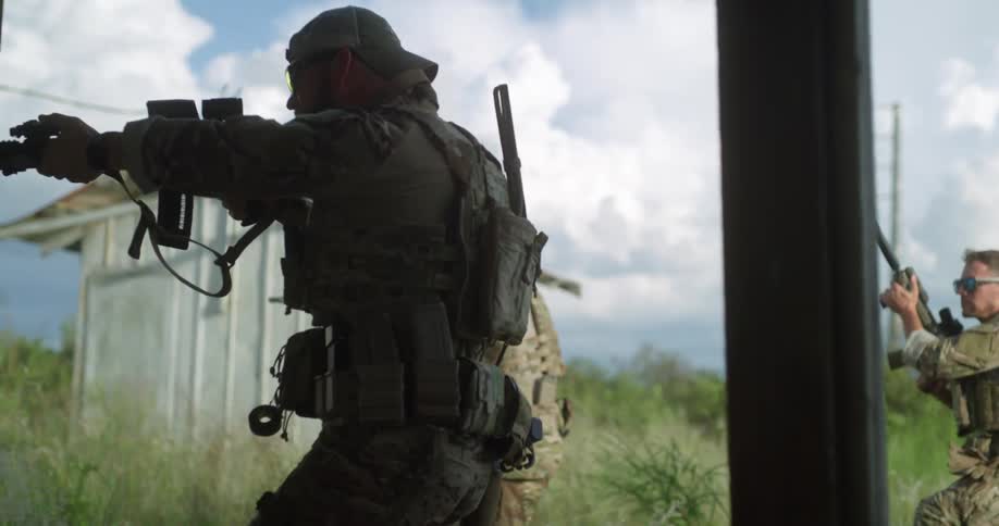 Two soldiers with their guns drawn slowly walk towards a building