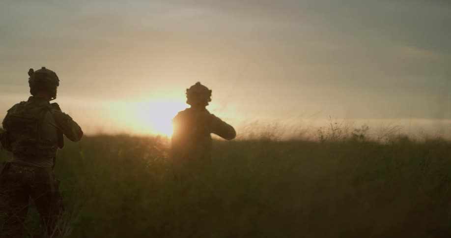 Two soldiers with their guns raised walks across a grassy field