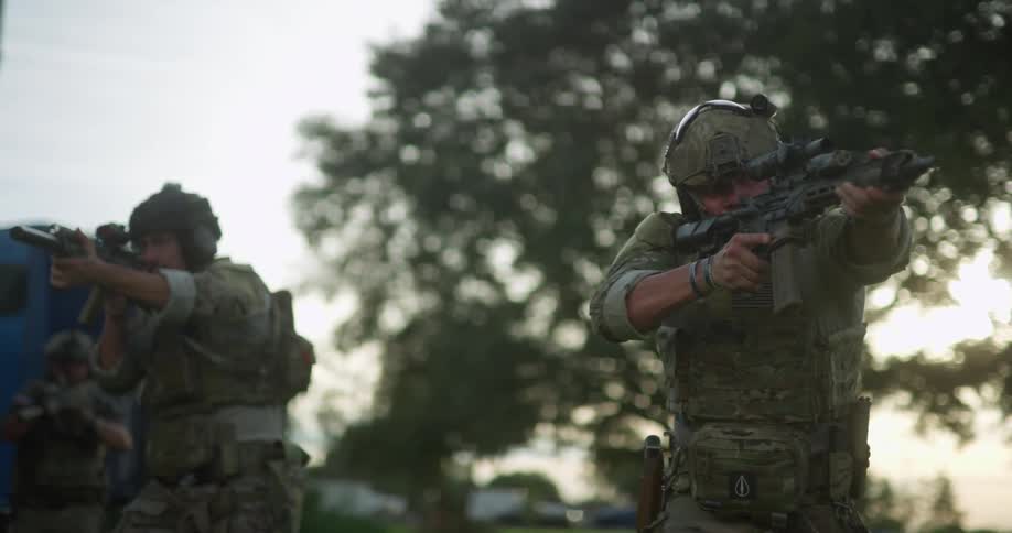 A group of armored soldiers with firearms on an outdoors practice exercise at sunset