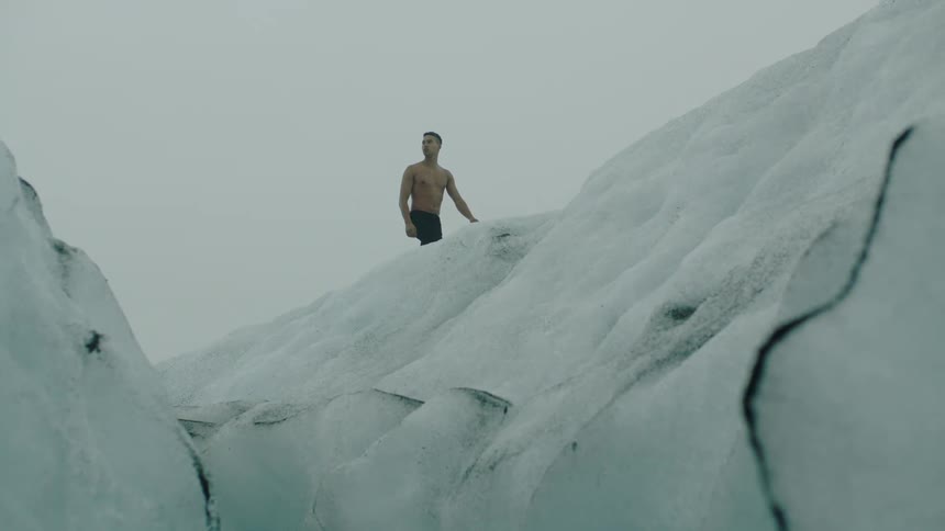 Shirtless fit young man walking over the ice covered top of a glacier