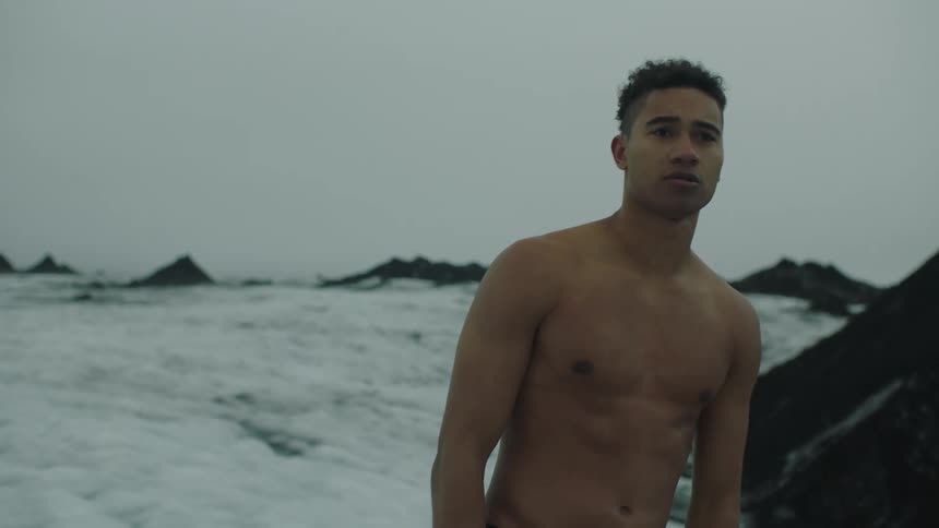 A young man without a shirt on stands on a snow covered field