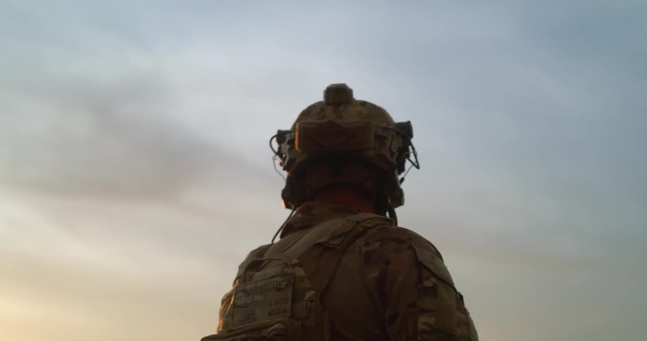 A military officer walking in army uniform with helmet and binoculars holding a guns