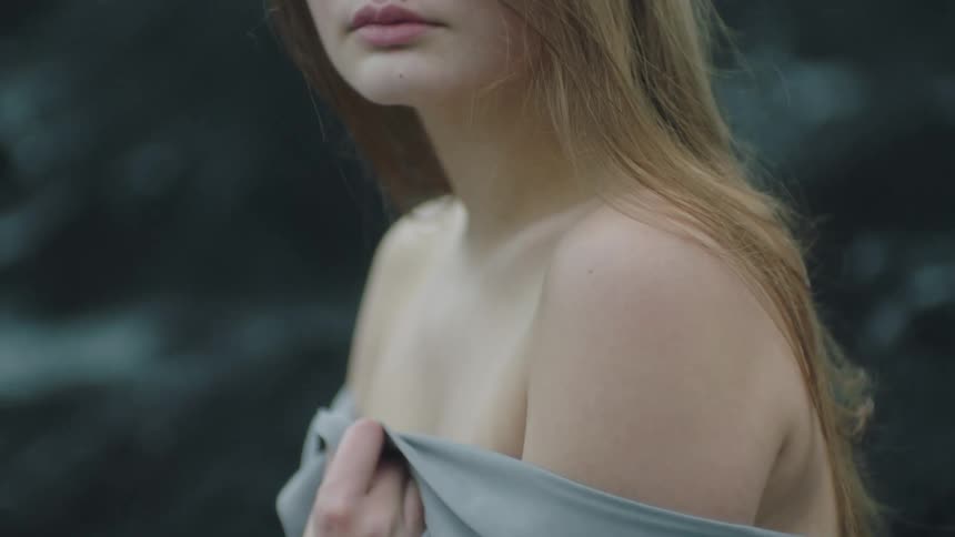 A young woman holds a sheet around her bare shoulders