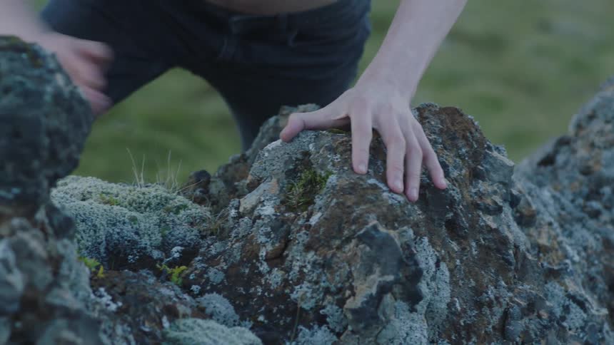 Young shirtless long haired man climbing rocks barefoot on the hills of the highland