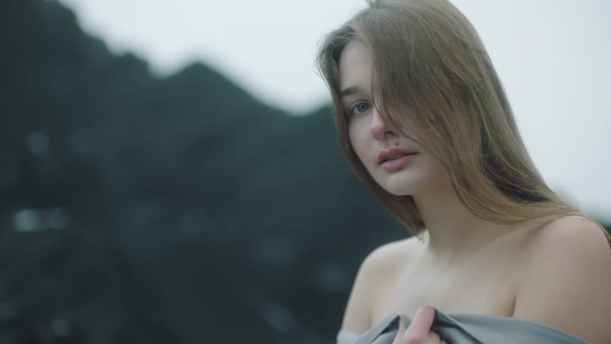 Young woman wearing a gray robe looking at the camera standing on near the mountains