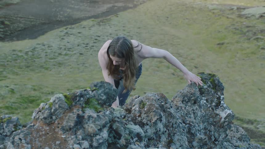 Shirtless long haired man climbing a rock on the highlands at day time