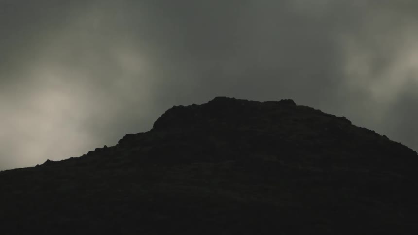 A hill with dirt and rocks with the sky and clouds in the background