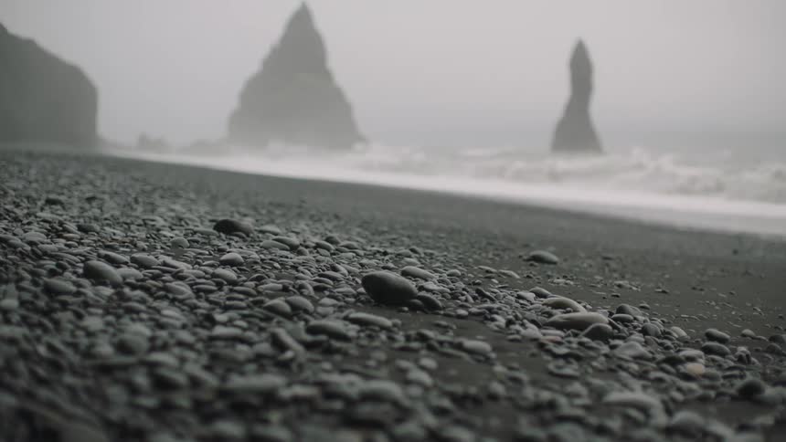 A beach with black sand and stones with the ocean the sky and clouds in the background
