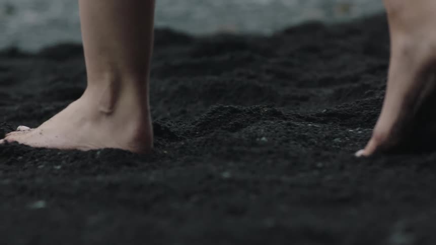 Barefoot young woman walking over the dark black sando on the beach