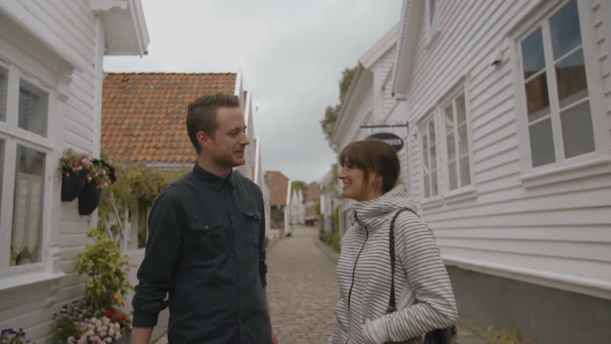 A man and woman stand between white cottage-style buildings and talk