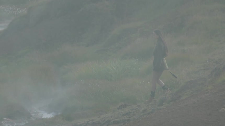 A teenage girl walks down a foggy hill towards a river