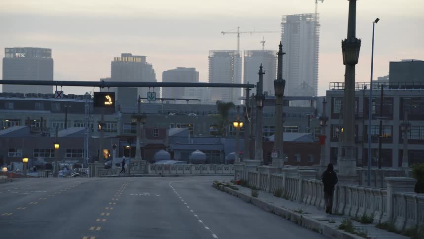 One person walks down a city sidewalk as another person jogs
