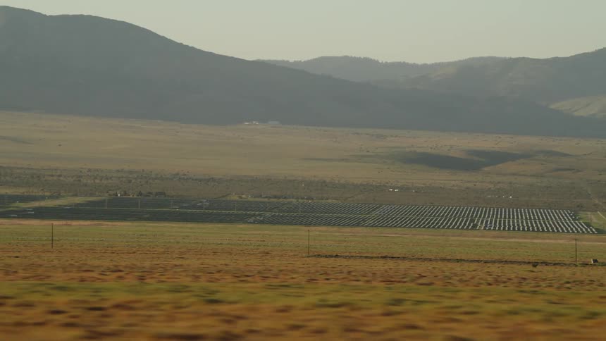 A grassy plain with a solar farm hills the sky and clouds in the background