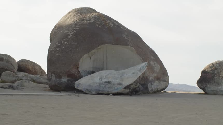 An immense fragmented boulder in the desert surrounded by smaller boulders