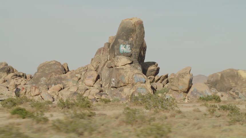 A rock formation covered in graffiti in an arid shrubland during the day