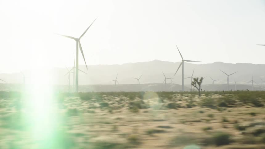 A wind farm in the desert with wind turbines with the sky and clouds in the background
