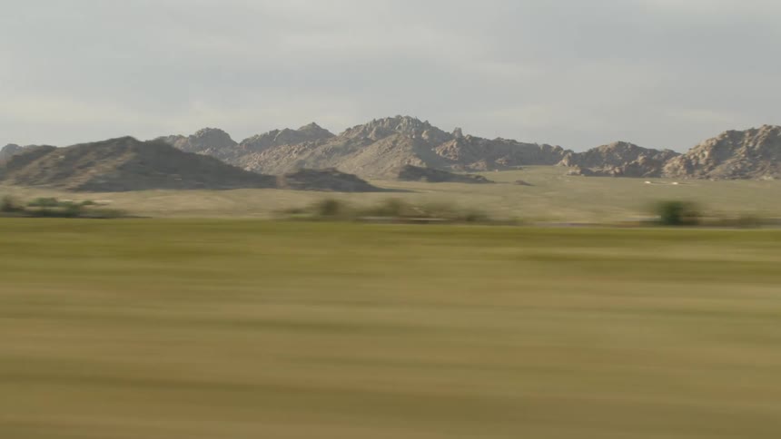A grassy plain with trees and a mountain range with the sky and clouds in the background
