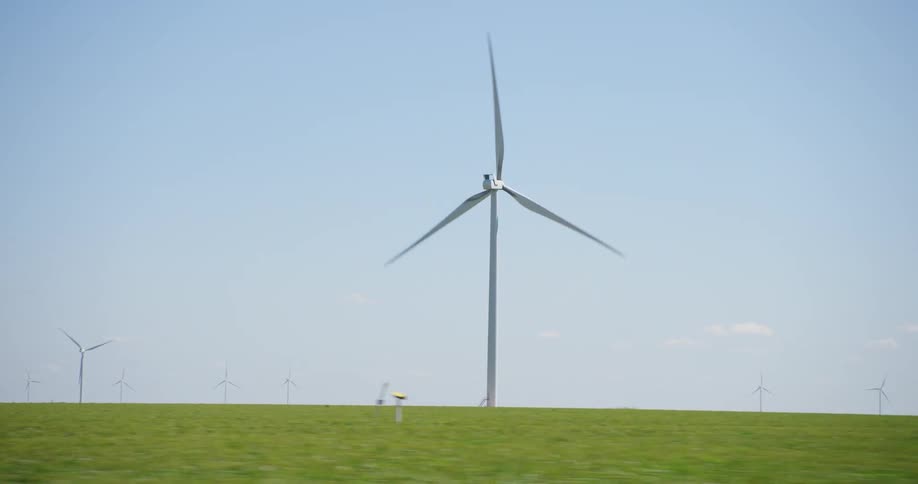 Wind turbines are in a field of green grass with a white truck driving near them