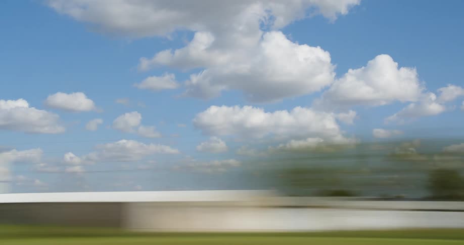 A grassy plain with trees and signs with the sky and clouds in the background