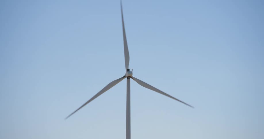 Wind turbine spinning against a blue sky at morning