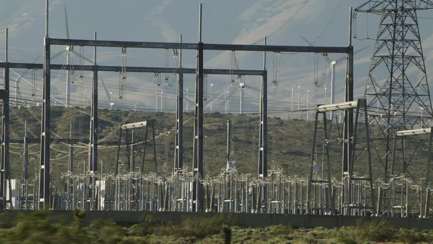 A power plant surrounded by wind turbines in a hilly countryside on a sunny day
