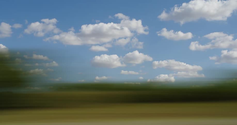 Country side speeds by on a bright sunny day with blue sky and fluffy clouds