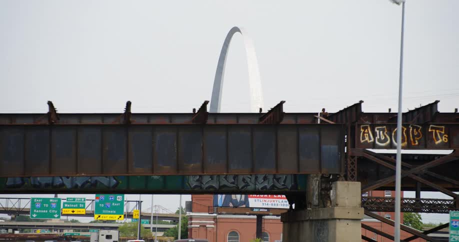 A highway with traffic signs train track overpass and the st louis arch