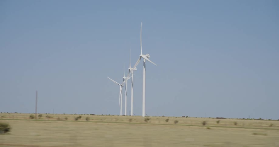 A row of wind turbines in a grassland next to a roadway on a sunny day
