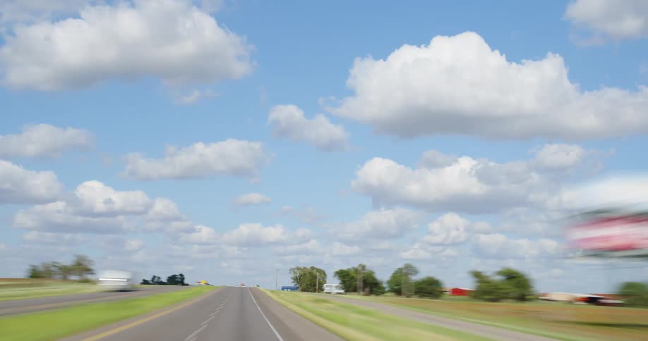 A highway with signs and vehicles with the sky and clouds in the background