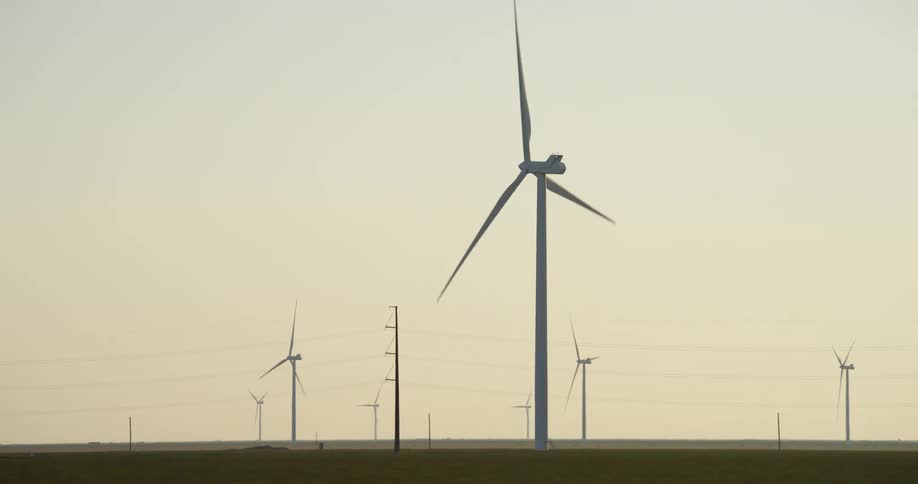 Trucks passing on a road next to a field with wind turbines at dusk