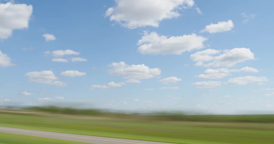 Time lapse of passing green fields in a rural area under the clouds on a blue sky
