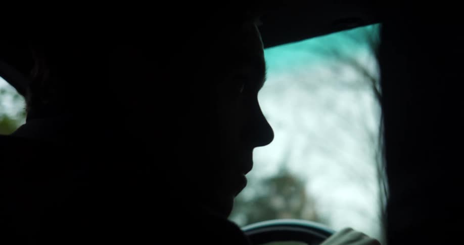 A man in profile drives a car looking to his right