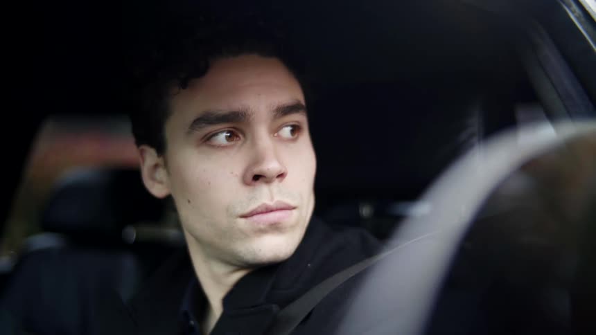 A man is driving in a car looking to his left while wearing a seat belt