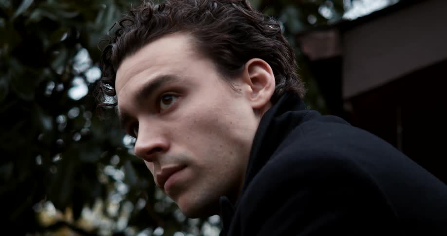 A young man under a tree outside looks in to the distance